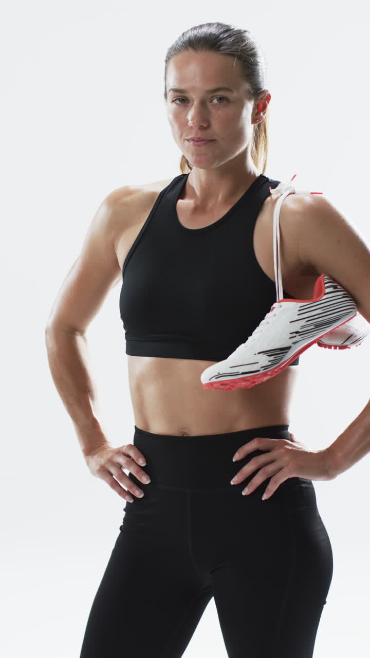 Vertical video: Caucasian female athlete holding running shoe, white background