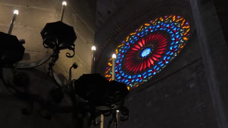 pan of stained glass window in cathedral with candle lit pillar in foreground