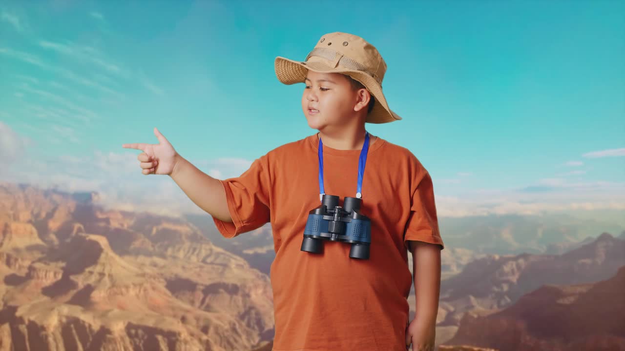 Asian Boy With A Hat And Binoculars Smiling And Pointing To Side While Traveling At The Top Of Mountain. Boy Researcher Examines Something, Travel Tourism Adventure Concept