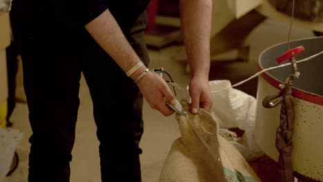 man opening bag of fresh coffee beans inside factory building, static shot