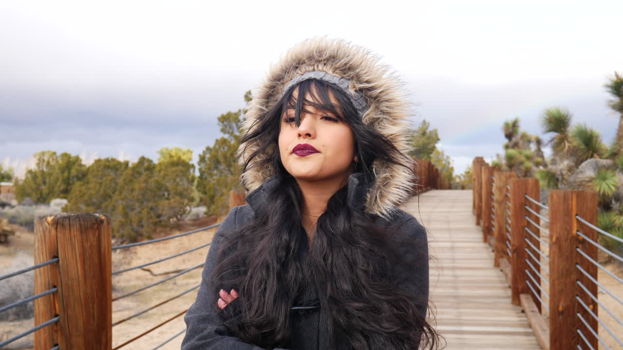 흐린 하늘 슬로우 모션 아래 폭풍우가 치는 나쁜 날씨에 사막의 다리에서 심각한 표정을 짓고 있는 아름다운 젊은 여성