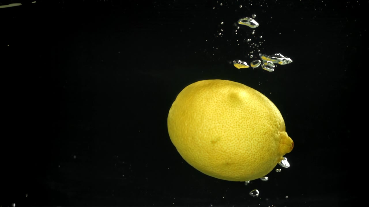 Limone giallo fresco che affonda lentamente nell'acqua con bolle su sfondo nero