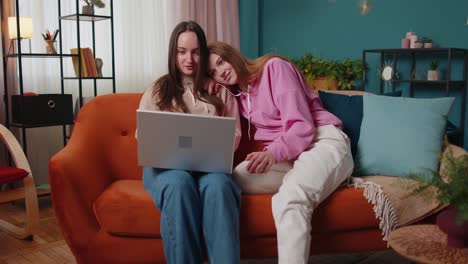 una pareja de mujeres jóvenes adultas mirando la pantalla de un portátil haciendo compras en línea en casa