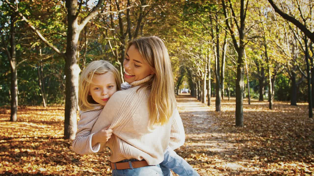 Junge Mutter lächelt, hält ihre kleine Tochter auf dem Arm und dreht sich während ihres Spaziergangs im Herbstpark im Kreis.