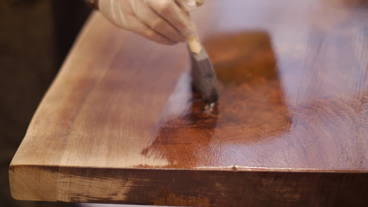 un artesano está terminando una mesa de madera natural hecha a mano con una capa de barniz en su tienda de madera