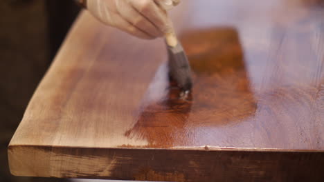 a craftsman is finishing a custom hand made natural wood table top with a coat of varnish in his wood shop