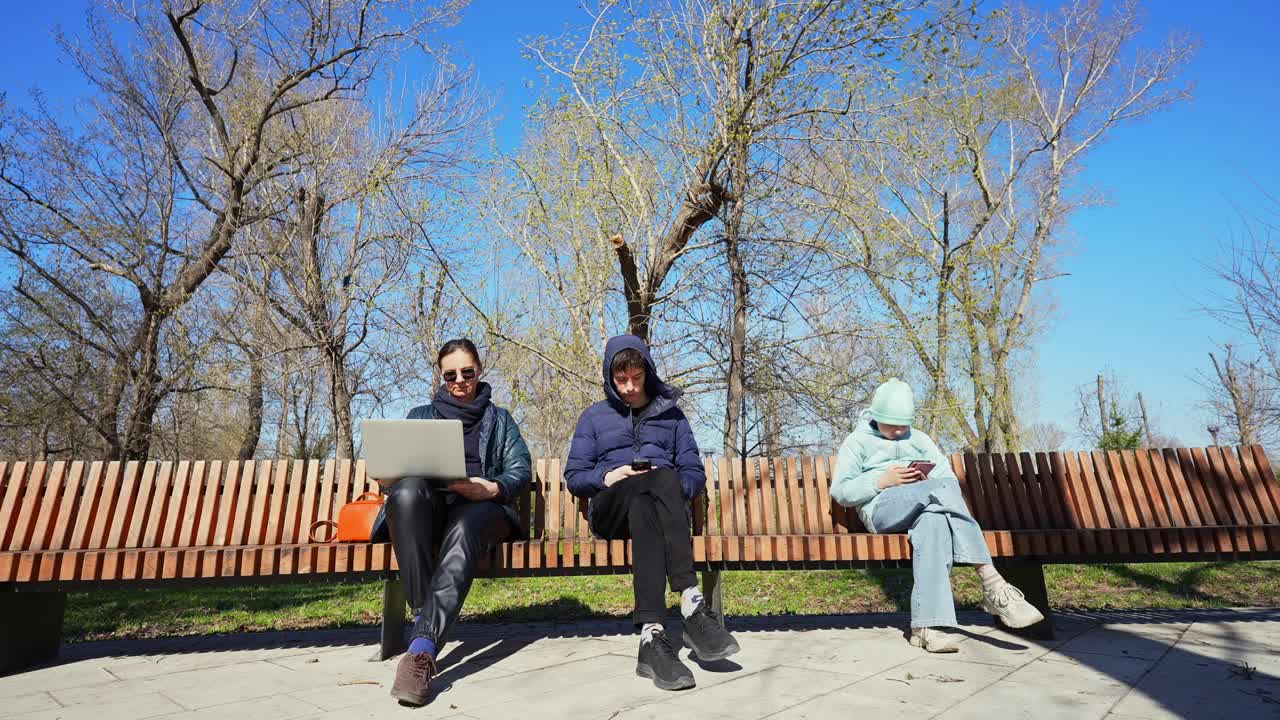 Tre persone usano un laptop e smartphone su una panchina del parco