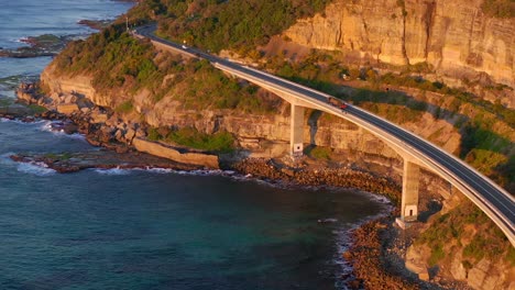 Vehículos-Que-Viajan-En-El-Puente-Del-Acantilado-Marino-Sobre-El-Océano-Azul-Tranquilo-Al-Amanecer-En-Nueva-Gales-Del-Sur,-Australia