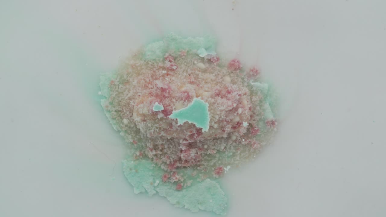 Colorful tablet dissolving in water, seen in close-up timelapse, creating soft texture