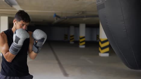 el hombre ejecuta fuertes golpes en la bolsa de boxeo en el gimnasio de la zona de estacionamiento, cámara lenta