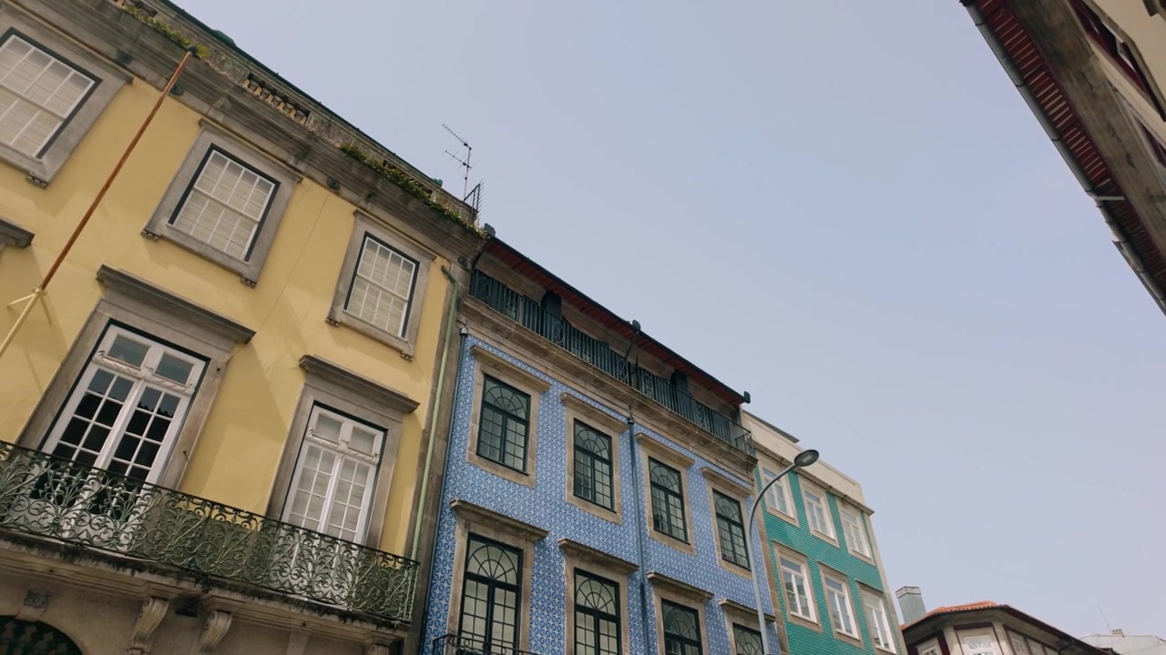 Vista ascendente de fachadas de edifícios históricos no Porto, Portugal, exibindo arquitetura europeia clássica. Destacam-se azulejos tradicionais e varandas decorativas sob um céu limpo.