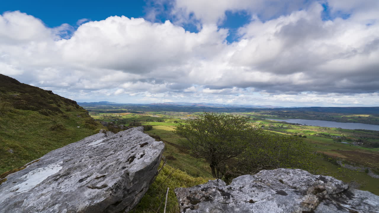 Timelapse of rural landscape with rock formation in the foreground and hills and lake in distance during sunny cloudy day viewed from Carrowkeel in county Sligo in Ireland