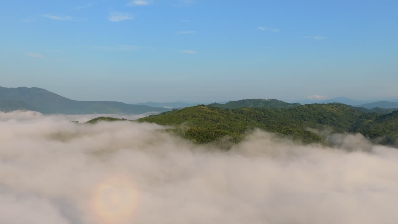 Drone footage captures the serene, fog-covered hills of Presa EL Carrizo, Tamazula de Gordiano, Jalisco. Lush greenery peeks through mist under a clear blue sky. Aerial beauty