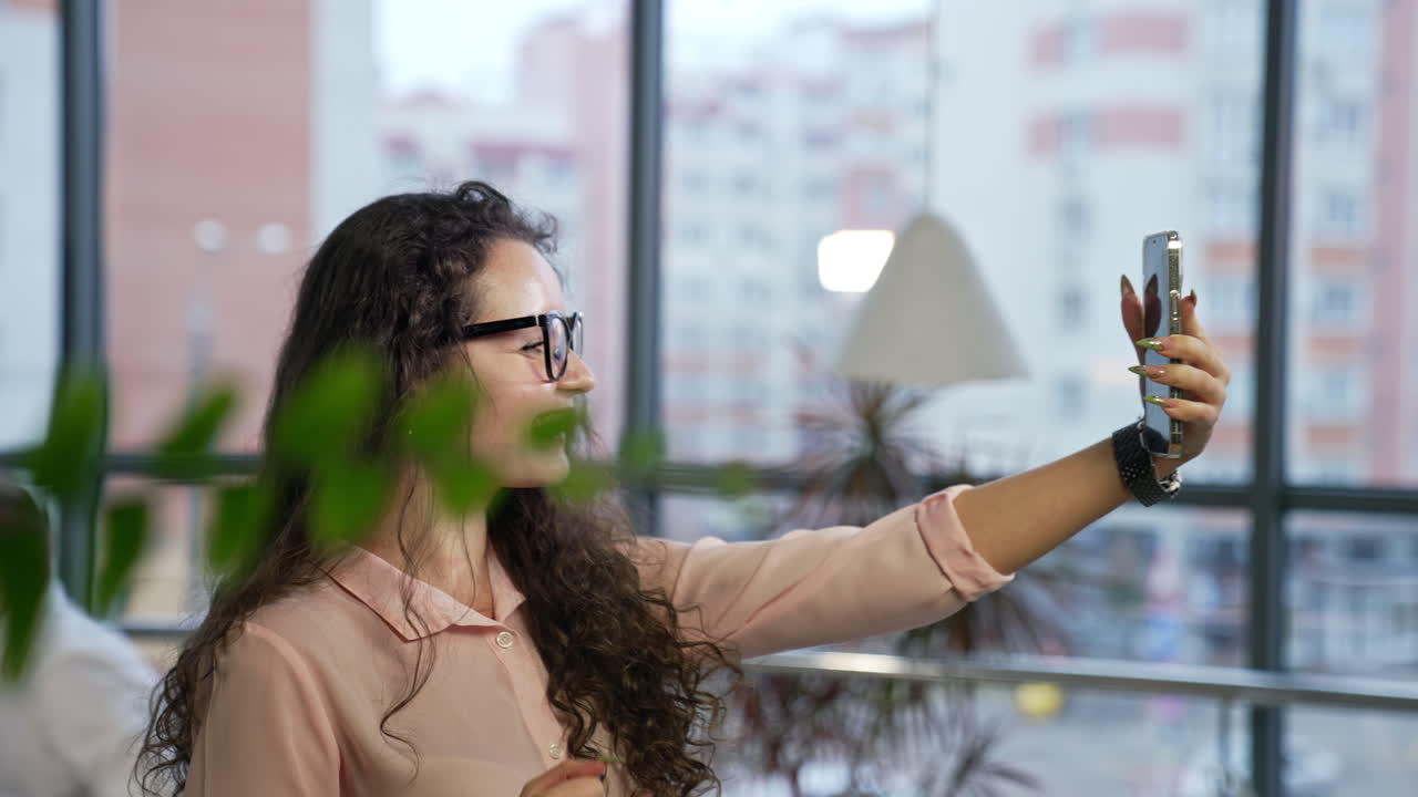Beautiful smiling lady having video call on her smartphone. Pleasant talk on the phone in an office with large windows.