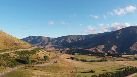 Scenic-aerial-drone-view-of-beautiful-countryside-shot-in-late-afternoon-on-a-clear-summer-day-with-tall-hills-in-the-background-and-green-fields