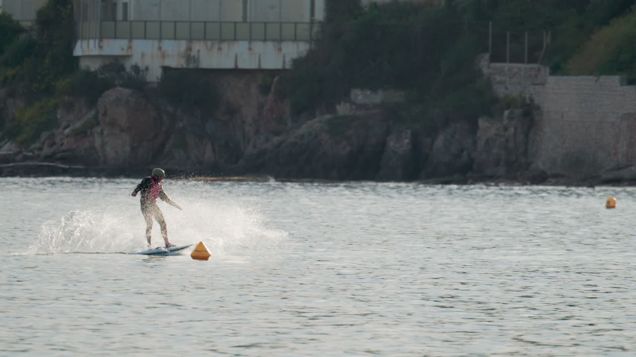Cannes, France - October 9, 2025: A surfer rides an electric foil board smoothly over the calm Mediterranean Sea near anchored boats