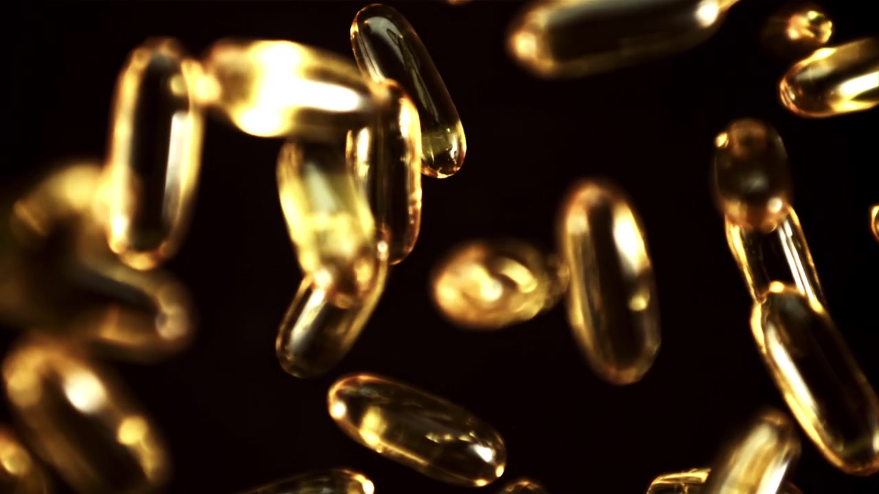 Capsule dorate di Omega-3 che cadono al rallentatore su sfondo nero