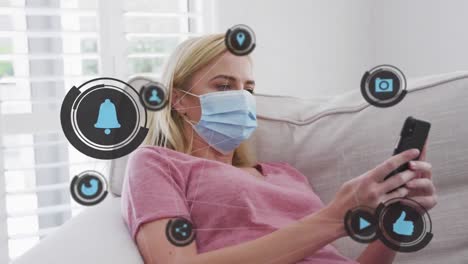 animación de iconos digitales sobre una mujer caucásica con máscara facial usando un teléfono inteligente en casa