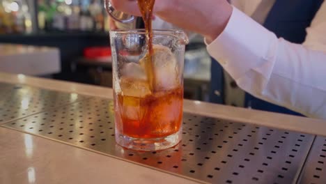 cocketeler pours martini with a jigger on a glass with ice