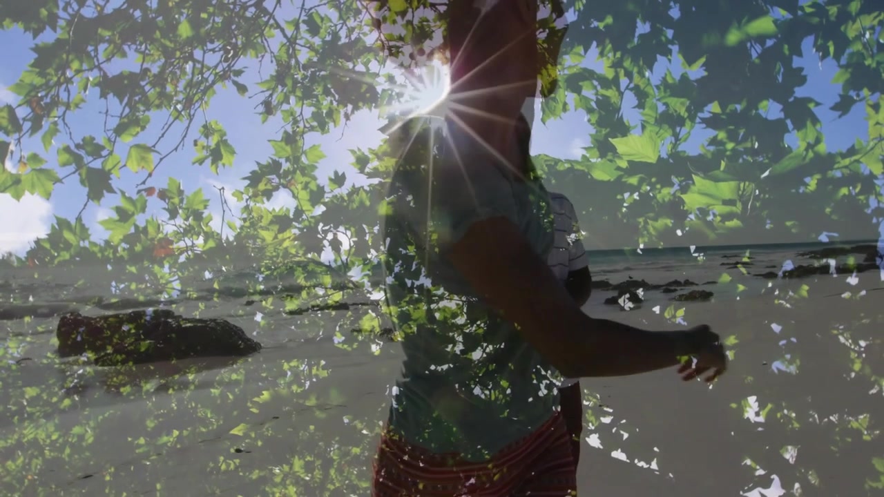 Couple walking on beach toward camera, camera shifting showing leaf overlay and sun flare for ads