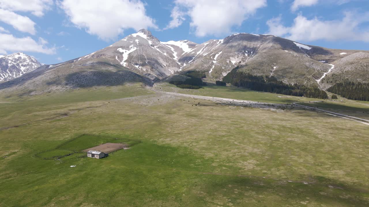 Vidvinkelbillede af et gammelt hyrdeskjul i en græslandsdal omgivet af Gran Sasso bjergkæden i Abruzzos landlige omgivelser i Italien
