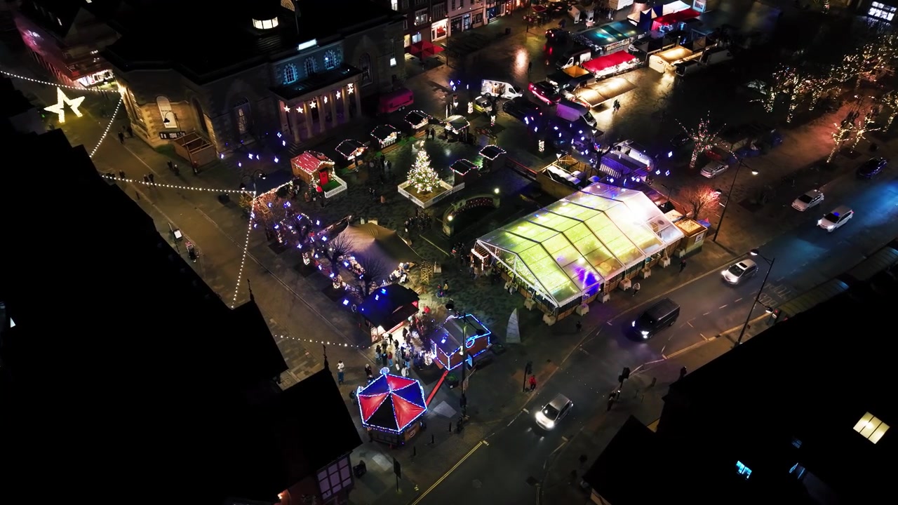 Luftdroneoptagelse om natten af Salisbury julemarked med markedsboder i glaspavilloner, et pyntet træ og forbipasserende trafik på den tilstødende vej.
