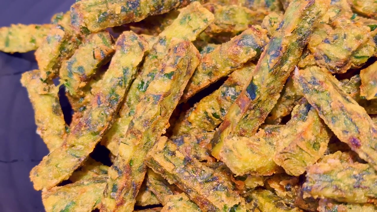 Primo piano di bastoncini dorati e croccanti di erba cipollina fritta disposti su un piatto, che mostrano una consistenza croccante e una presentazione da street food salato in stile asiatico.