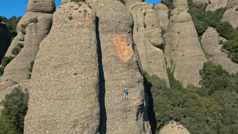 aerial-view-of-a-climber-climbing-a-needle-in-the-montserrat's-mountains,-with-an-upward-camera-movement