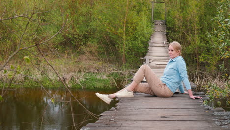 woman sitting on old wooden bridge over a river in a forest