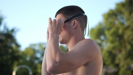 young attractive swimmer puts on his swimming goggles side profile medium shot