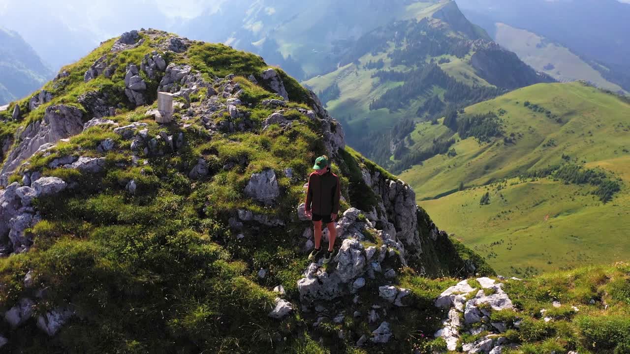un joven con capucha y gorra está parado en el borde de la cima, mirando el asombroso y dramático paisaje
