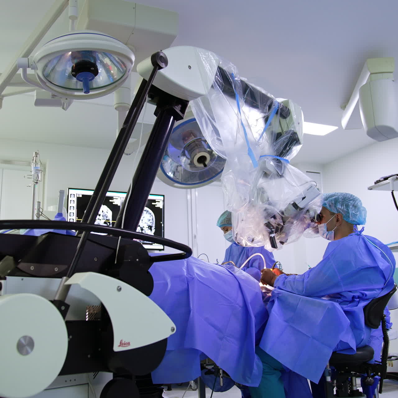 Modern well-equipped surgery room with advanced equipment. Doctor sits at operational table looking at microscope.