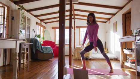 Mujer-Relajada-De-Raza-Mixta-Practicando-Yoga,-De-Pie-Y-Estirándose-En-El-Soleado-Dormitorio-De-La-Cabaña