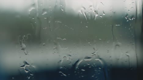 Regen-Auf-Fensterglas-Mit-Verschwommenem,-Stimmungsvollem-Hintergrund,-Handaufnahme