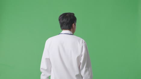 back view of asian male doctor with stethoscope looking around and walking on green screen background in the hospital