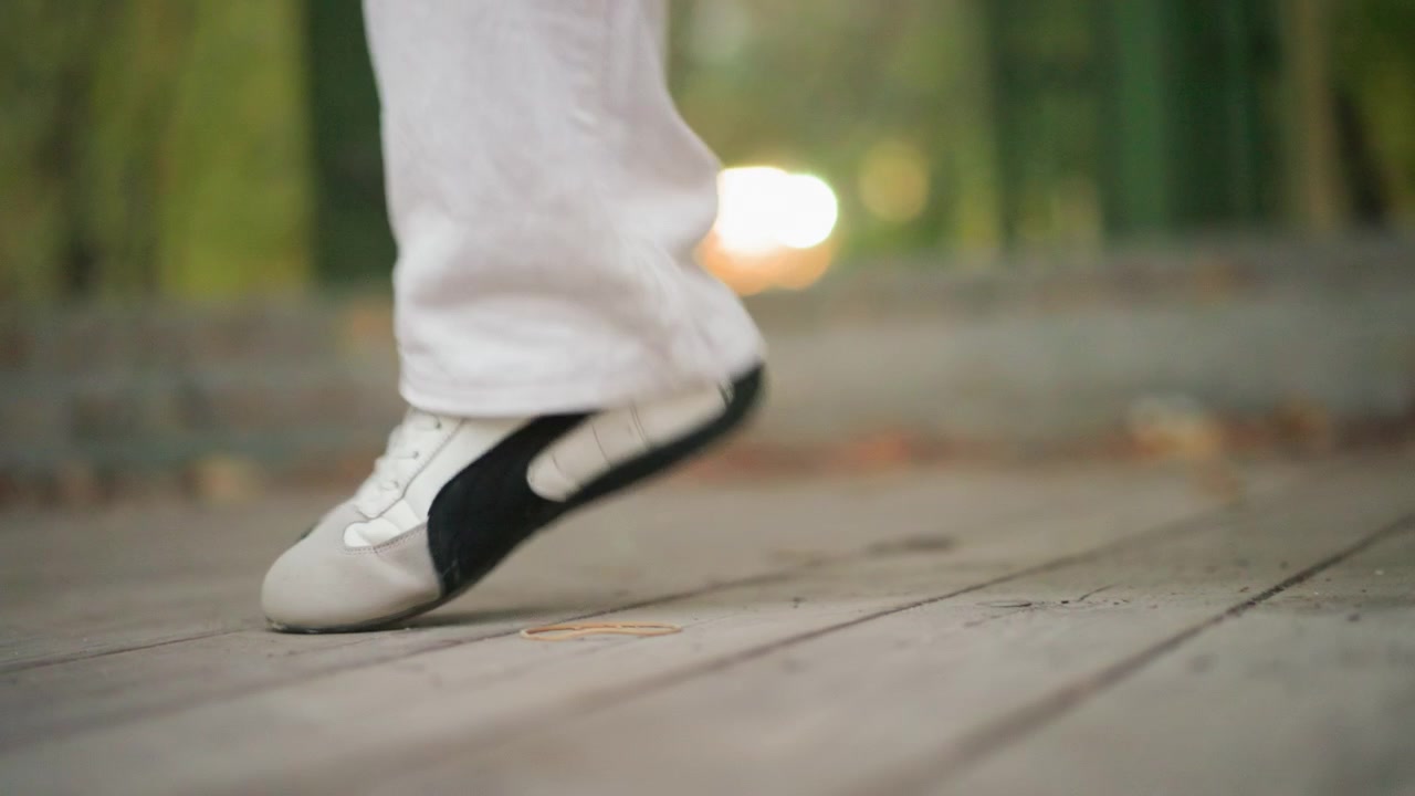 Close up of person performing dance steps with precise footwork on wooden floor. Foot movements are captured in detail showing controlled motion and balance. Background is softly blurred