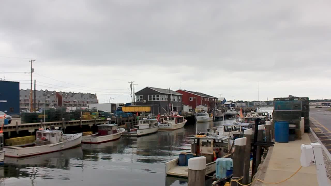 Lobster Boats sit idle in Portland Harbor, Maine with building and lobster pots on the sides.