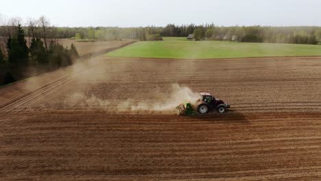 spring tractor plows dry soil as drone flies leftward in dusty latvian field