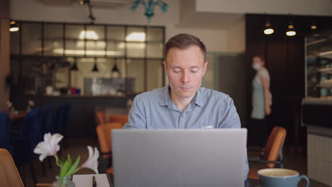 A-young-man-in-a-shirt-is-sitting-at-a-table-with-a-laptop-and-typing-on-the-keyboard.-A-student-can-study-remotely.-A-businessman-conducts-his-business-remotely