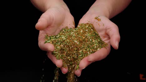 toma estática de manos de mujer dejando caer deliciosas especias con albahaca, pimienta y perejil contra fondo negro en cámara lenta