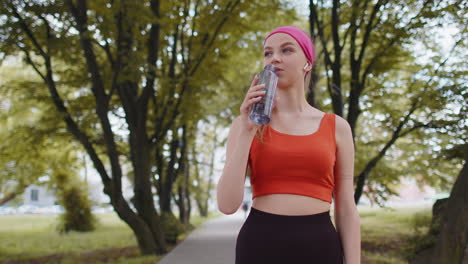 Corredor-Deportivo-En-Forma-Atlética-Niña-Bebiendo-Agua-De-La-Botella-Después-De-Entrenar-Haciendo-Ejercicio-En-El-Parque