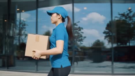 a diligent delivery person in a blue uniform carrying a package while walking confidently through a modern building entrance on a sunny day, showcasing efficiency and professionalism