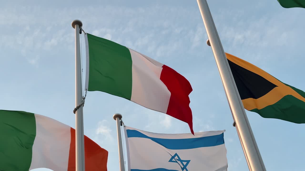 A low-angle view of the Italian flag waving gracefully in the wind among other flags under a bright blue sky, symbolizing Italy’s national pride and presence on the global stage