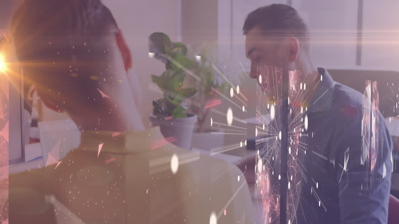 At desk, two people working with fireworks animation overlaid on screen