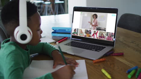 african american boy doing homework while having a video conference on laptop at home