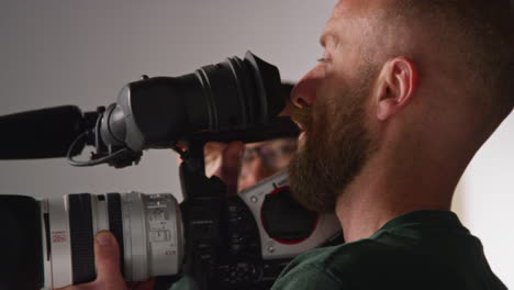 male film camera operator taking camera off tripod to shoot handheld movie or video in studio 1