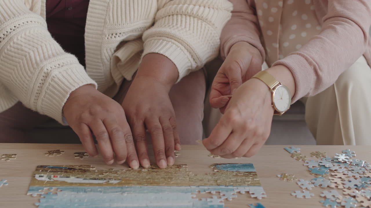 Steadicam of hands of cropped unrecognizable people sitting at coffee table, doing puzzle