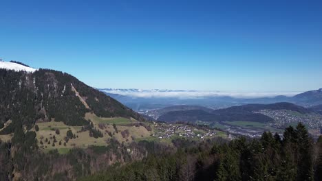 Drone-fly-between-pine-trees-revealing-beautiful-mountain-cityscape-in-Vorarlberg,-Austria