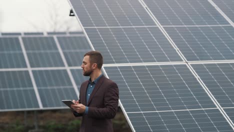 Un-Hombre-De-Negocios-Con-Una-Chaqueta-Y-Una-Tableta-Inspecciona-Una-Planta-De-Energía-Solar