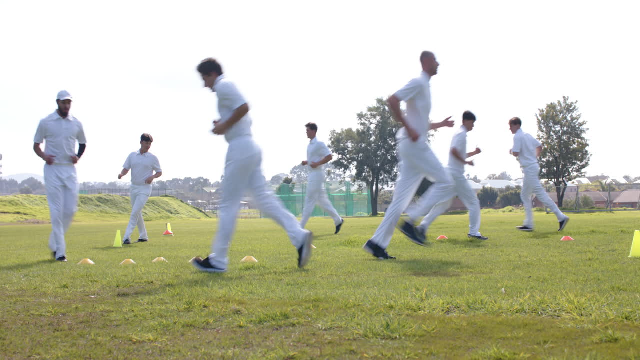 Team of multiracial male cricket players practicing cricket wearing cricket whites on pitch